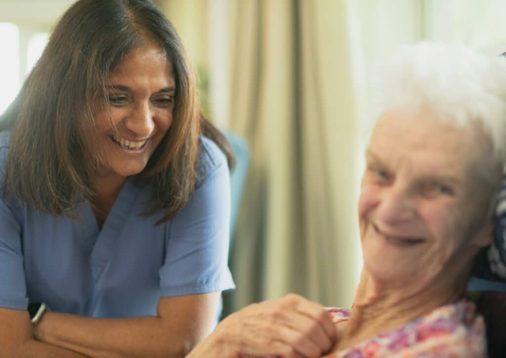 Una caregiver conversa sorridendo con una donna anziana, immagine legata alla relazione di cura e al sostegno.