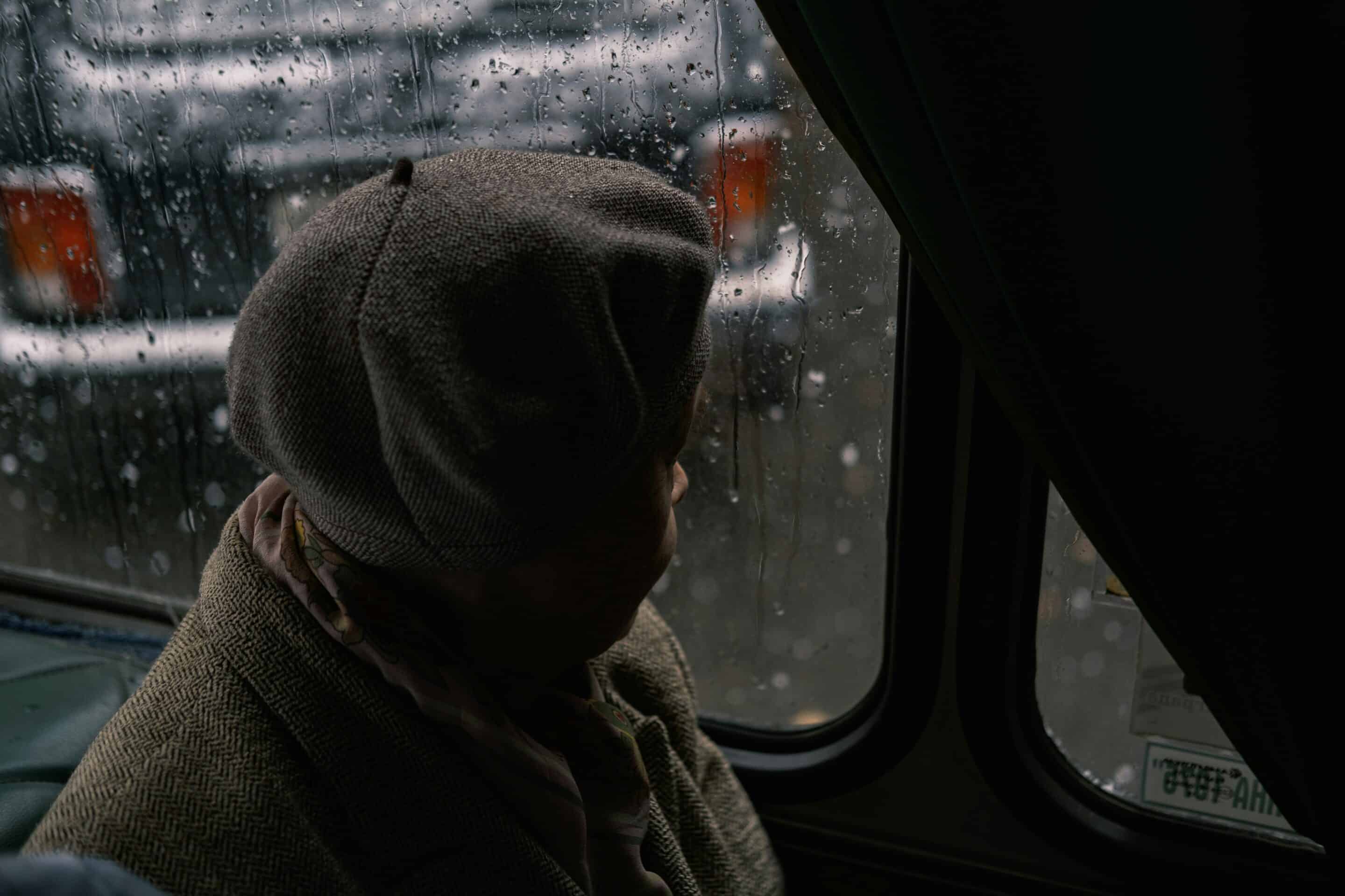 Persona avvolta in una coperta guarda fuori da una finestra in una giornata piovosa, immagine legata alla SAD e al cambiamento stagionale.