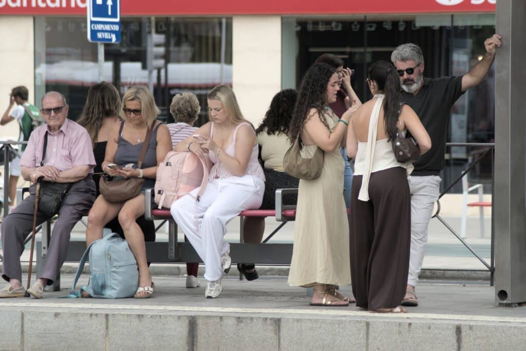 Persone in attesa alla fermata dell’autobus, alcune delle quali controllano il telefono per passare il tempo.