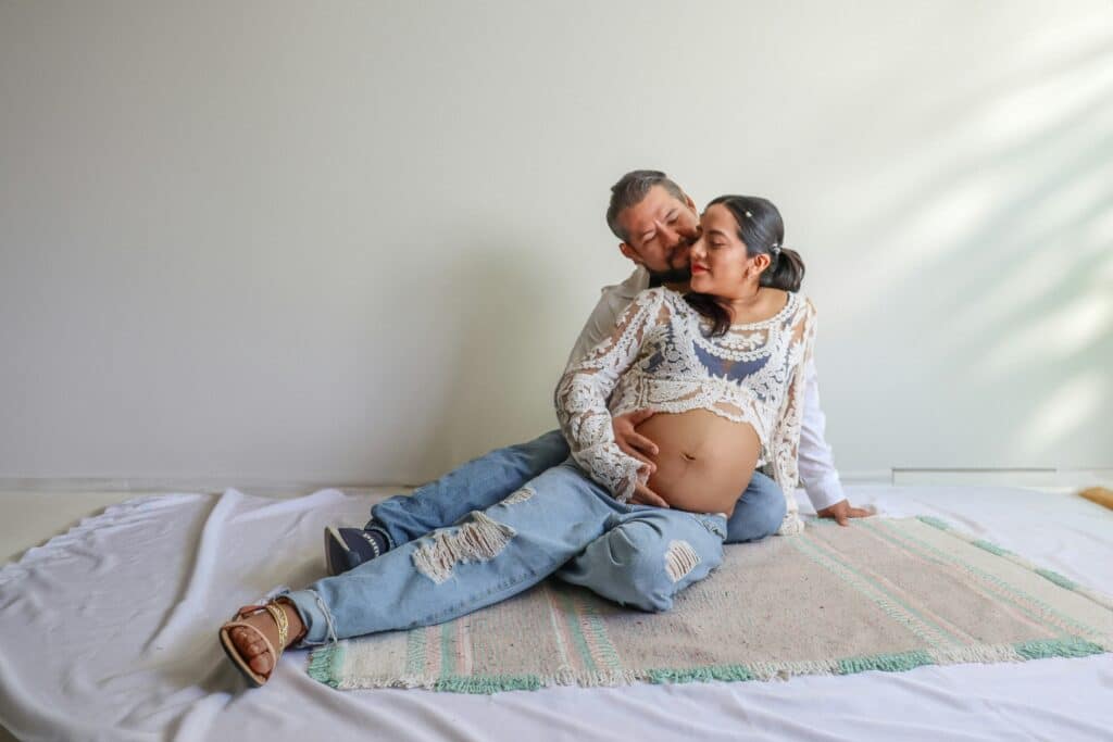 Coppia in gravidanza abbracciata sul letto, immagine legata alla sessualit&agrave;, all&rsquo;intimit&agrave; e al sostegno del partner.