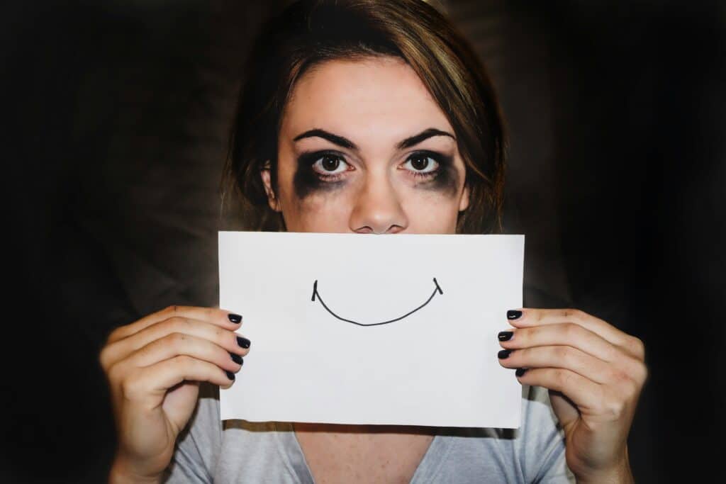 Donna che nasconde parte del volto dietro un foglio con un sorriso disegnato, immagine simbolica delle emozioni tenute a distanza attraverso il rimuginio.